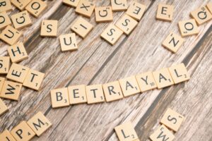 Wooden letter tiles spelling 'Betrayal' on a rustic wooden surface, conveying themes of deceit and dishonesty.