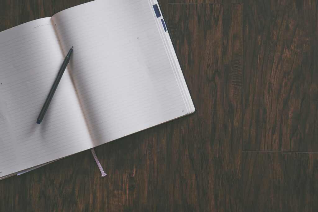 An open notebook with a pen resting on a wooden desk, ideal for productivity themes.
