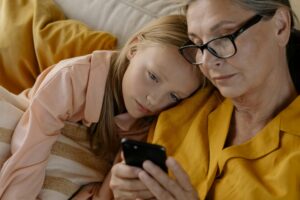 A grandmother and granddaughter sharing a bonding moment while looking at a mobile phone indoors.